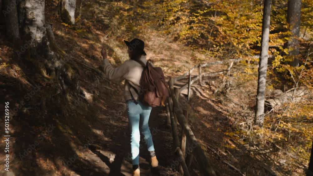 rear view Woman tourist walks on trail in autumn woods at sunny day. female ukrainian hiker in hat with backpack hiking in forest around mountain lake Sinevir, Ukraine. rear view Woman tourist walks on trail in autumn woods at sunny day. female ukrainian hiker in hat with backpack hiking in forest around mountain lake Sinevir, Ukraine.