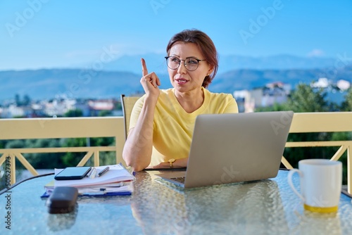 Middle aged woman in home office looking at laptop screen, talking on video call