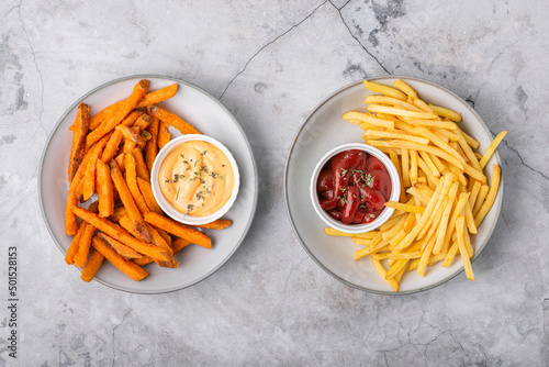 Two plates full of sweet potato fries and French fries with sauces, top view