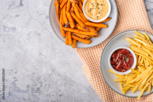 Baked sweet potato fries and French fries on plates over concrete background, top view