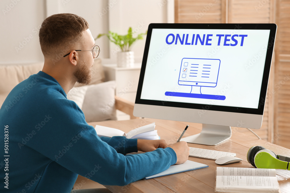 Man taking online test on computer at desk indoors Man taking online test on computer at desk indoors