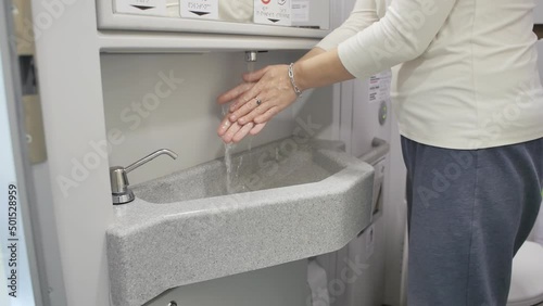 A young female train passenger has entered the restroom and washes her hands using liquid soap and tap water. Modern comfortable high speed train photo