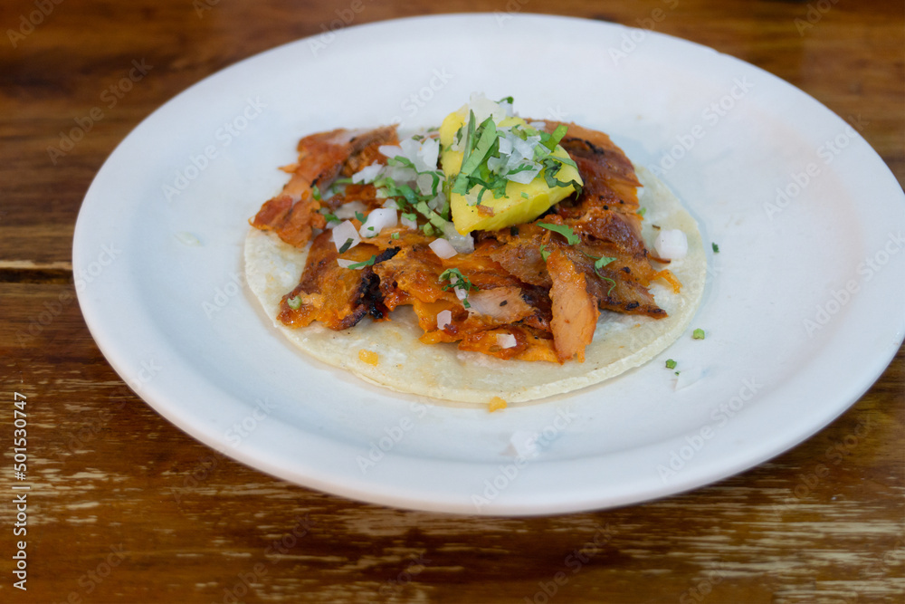 One taco with pork on a plate. Tacos with meat onions, greens and lemon. Traditional Mexican cuisine. One taco with pork on a plate. Tacos with meat onions, greens and lemon. Traditional Mexican cuisine.