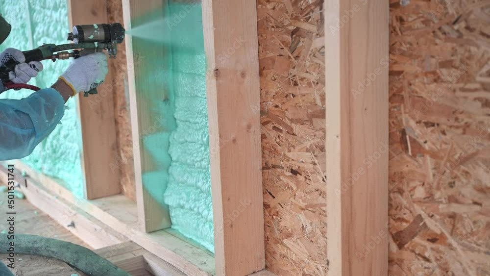 Male builder insulating wooden frame house. Man worker spraying polyurethane foam inside of future cottage, using plural component gun. Construction and insulation concept. Male builder insulating wooden frame house. Man worker spraying polyurethane foam inside of future cottage, using plural component gun. Construction and insulation concept.