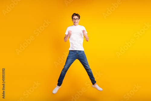 Full body photo of young cheerful man rejoice victory fists hands jump isolated over yellow color background