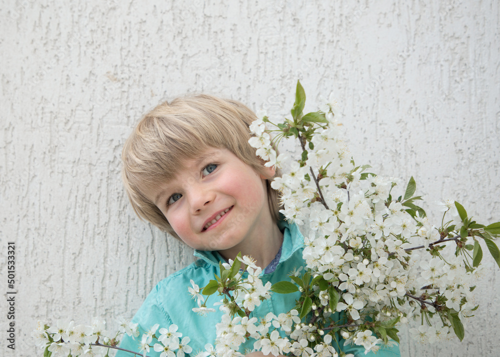 portrait of a cute positive blond boy 5 years old in a turquoise shirt with a bouquet from a branch of cherry blossoms
