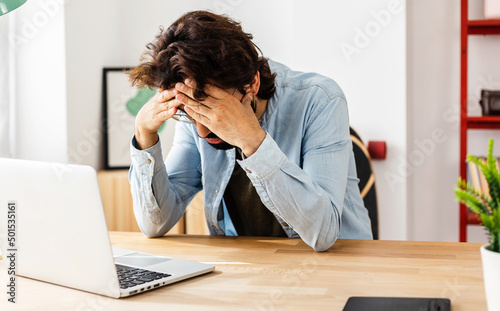 Young professional freelancer man looking worried and stressed over work while sitting on a desktop at home office. Business concept. photo