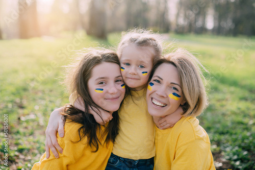 Portrait of Ukrainian family. Mom with two little daughters hugging and smiling in nature on sunny day.