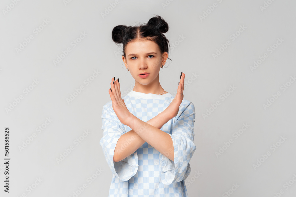 Serious dark-haired teen girl crossing arms and palms doing negative sign, prohibit, forbid smth bad, standing in trendy t shirt over light grey background. Social distancing Serious dark-haired teen girl crossing arms and palms doing negative sign, prohibit, forbid smth bad, standing in trendy t shirt over light grey background. Social distancing