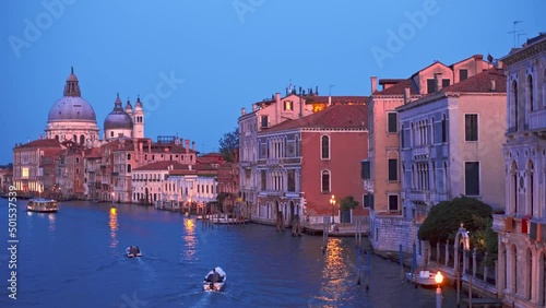 View of Venice Grand Canal with boats and Santa Maria della Salute church in the evening from Ponte dell'Accademia bridge. Venice, Italy. Horizontal camera pan