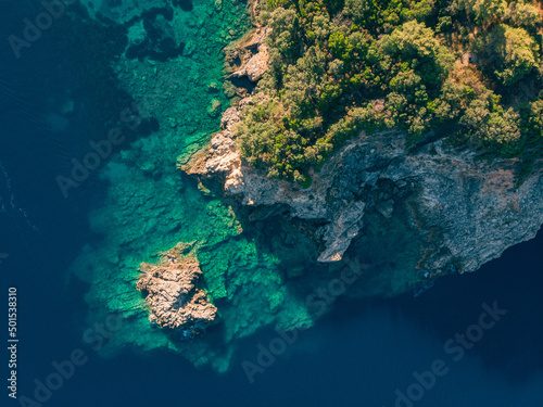 Rocky shore of Adriatic Sea covered with trees. Crystal clear turquoise water. Top down view.