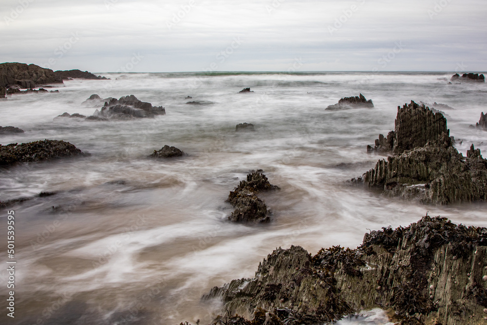 Dramatic black rocks break through the surf on a North Devon beach.  A slow shutter speed brings a dreamy effect.