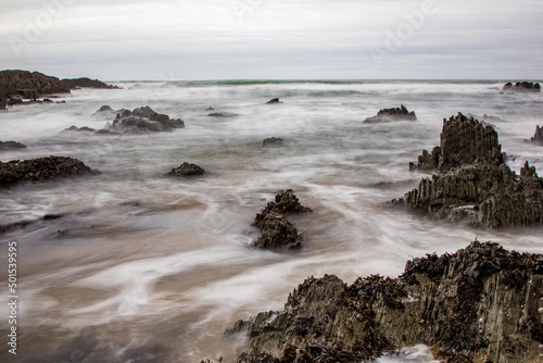 Dramatic black rocks break through the surf on a North Devon beach. A slow shutter speed brings a dreamy effect.