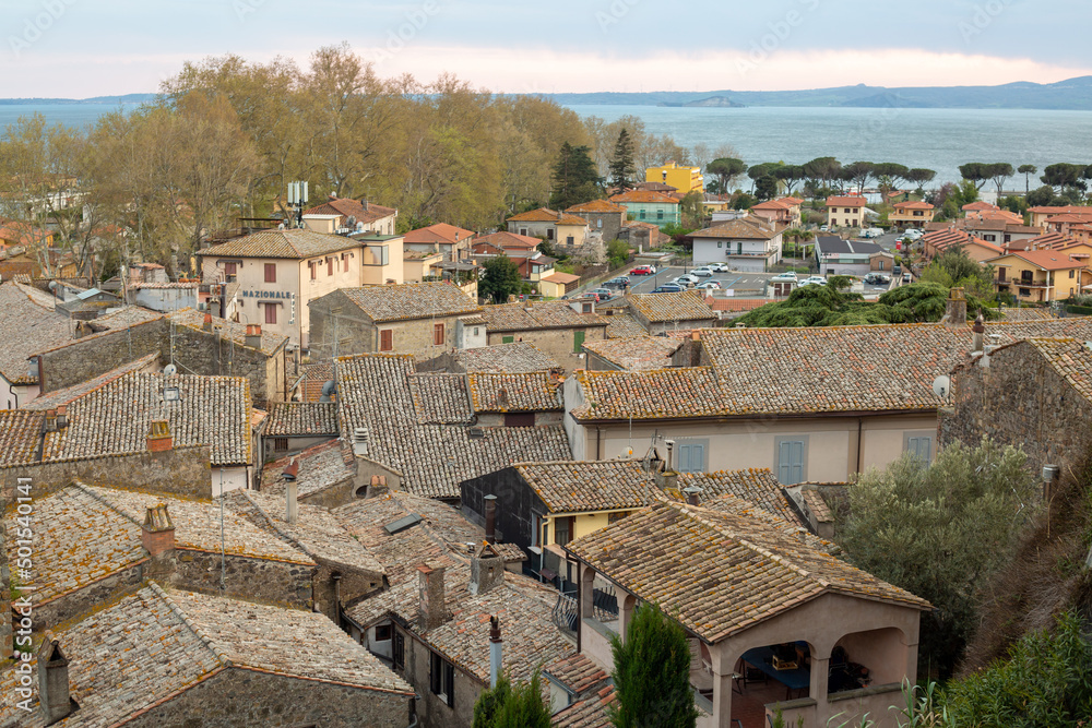 Panoramic aerial view of the old famous city of Bolsena and Lake Bolsena at sunset. Province of Viterbo, Italy, Lazio. Cityscape and tiled roofs