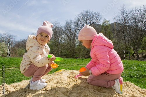 Adorable little girls have fun on the playground in the sandbox. Children play with sand molds and make Easter cakes. Creative outdoor activities for children. Girls in the sandbox outside