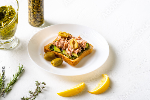 toast with tuna and avocado, olives with chimichurri sauce. On a white plate and white background.