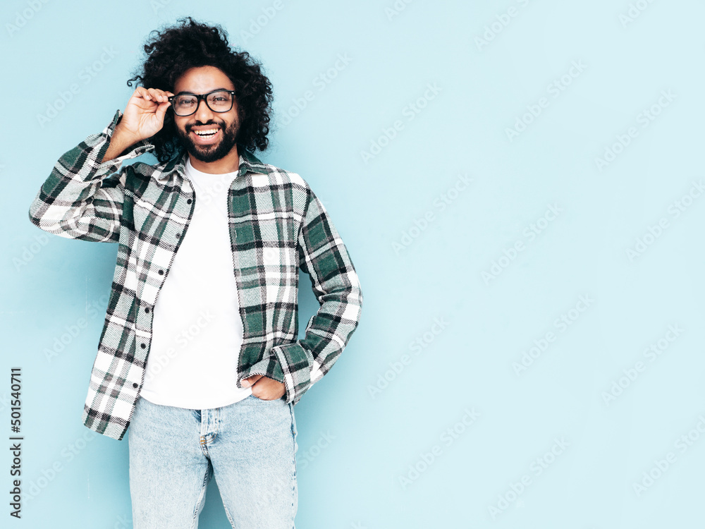Handsome confident hipster  unshaven Arabian man dressed in summer  shirt and jeans clothes. Fashion male with long curly hairstyle posing near  blue wall in studio. In spectacles Stock Photo | Adobe