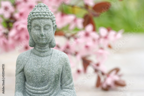 Buddha statuette against blurred blooming sakura branch as background with copy space. Meditation and spa concept, mental health. Time for yourself