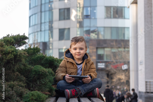 little boy having fun using a smartphone sitting on bench on the background of office building.front view image