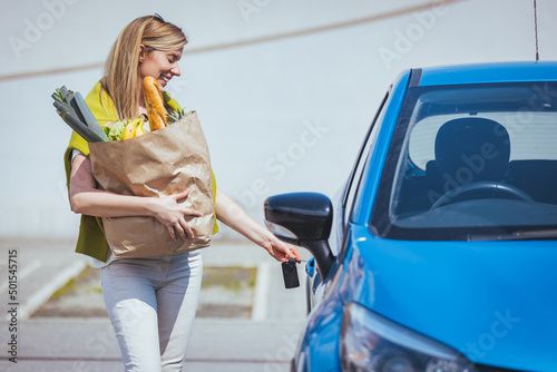 Young woman riding shopping cart full of food on the outdoor parking. Young woman in car park, loading shopping into boot of car. Shopping successfully done. Woman putting bags into car after shopping