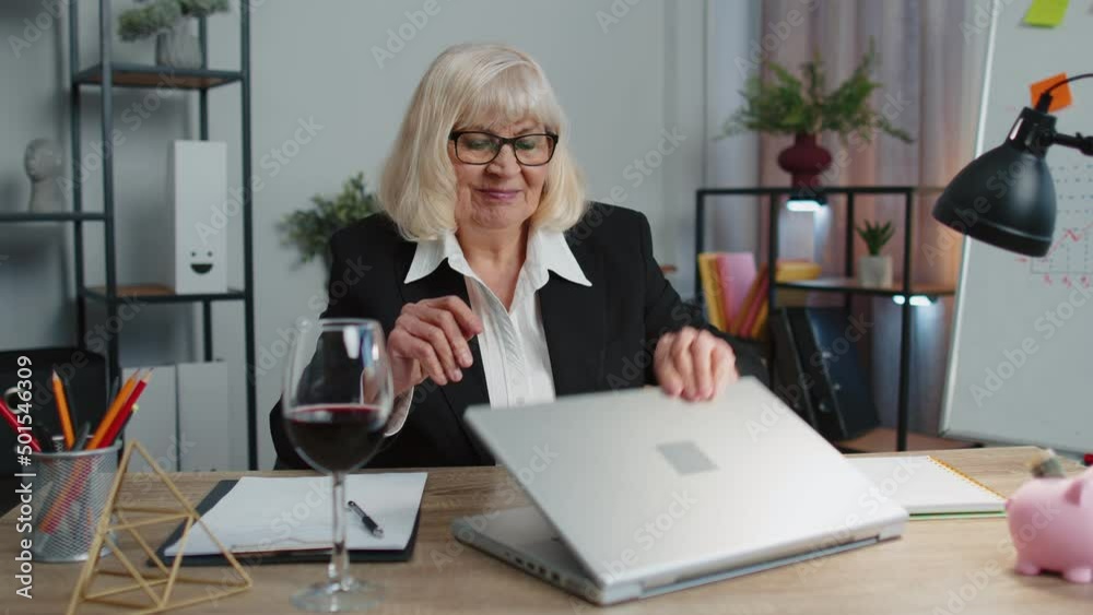 Senior woman freelancer drinking wine from glass after working on laptop computer pc sitting at desk at home office. Elderly mature granny e-learning, online distant video call conversation remote job