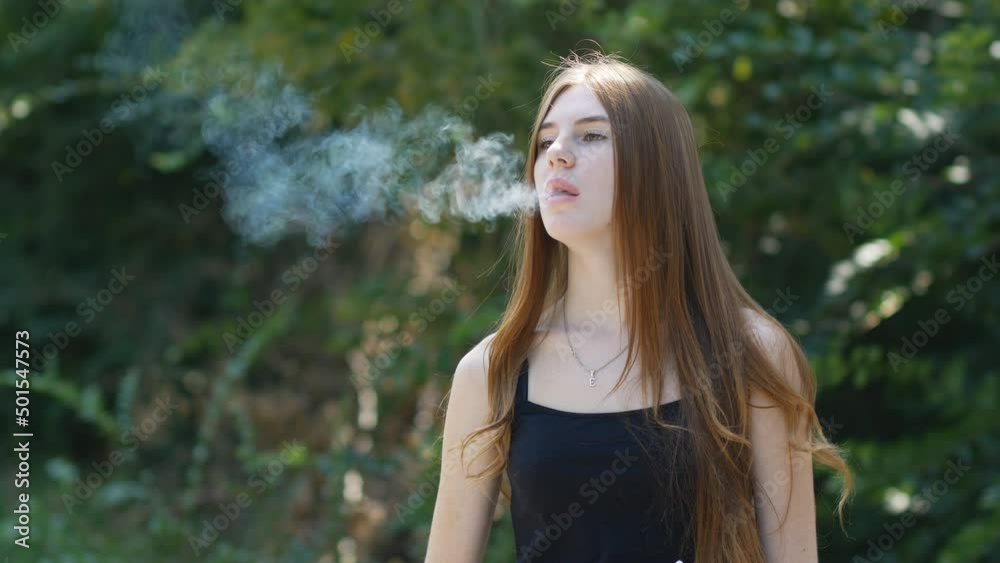 Portrait of a young girl smoking a vape. IQOS. Woman puffs on a vape pen. Blowing smoke out of your mouth is delicious. Portrait of a young girl smoking a vape. IQOS. Woman puffs on a vape pen. Blowing smoke out of your mouth is delicious.
