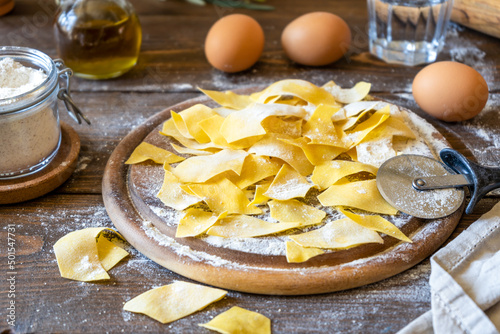 Homemade pasta Maltagliati on cutting board with ingredients on wooden background. Close up