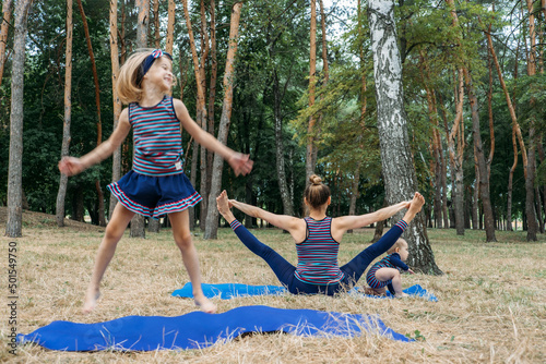 Parents and mental health. Parents zen. Little preschool daughter jumping while her mother doing yoga sitting on lotus position in park. Excited girl playing near meditating mother.