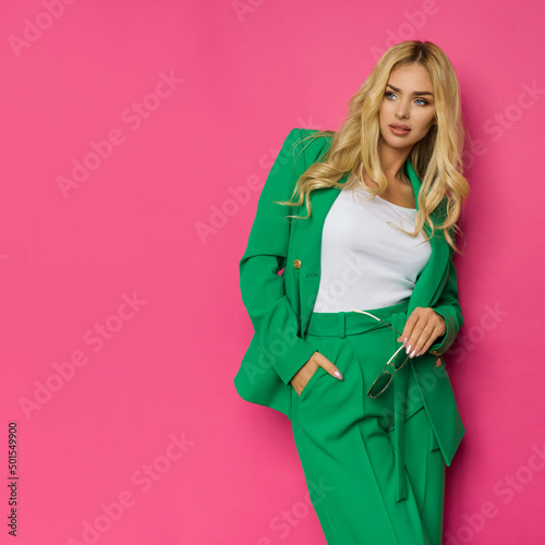 Beautiful blond woman in unbuttoned green jacket and pantsuit is posing with hand in pocket. photo