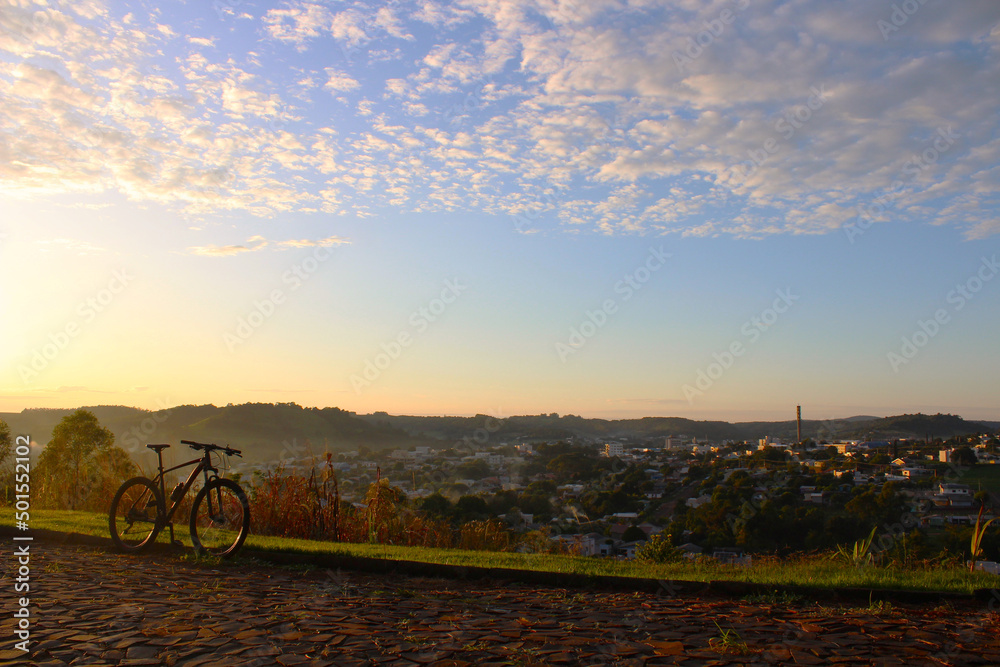 Foto do amanhecer na cidade com poucas nuvens e a bicicleta na lateral, Salto do Lontra - PR, 17 de abril de 2022