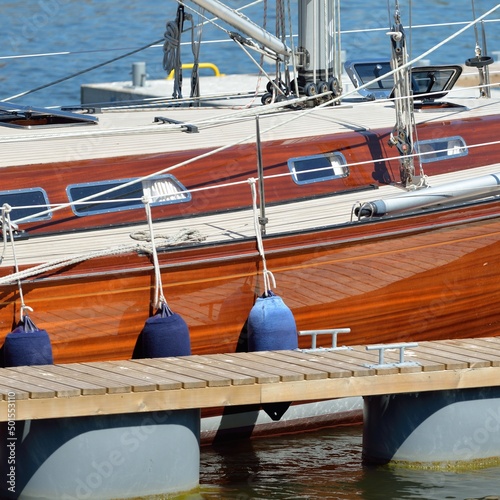 Elegant modern sailing boat with wooden teak deck moored to a pier in a yacht marina. Nautical vessel, transportation, sport, regatta, recreation, leisure activity, cruise, vacations, lifestyle themes