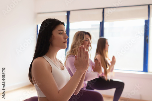 Group young attractive people practicing yoga lesson with instructor, standing together in Virabhadrasana exercise. Caucasian female coach trains pose for girls. Indoor portrait, studio background.