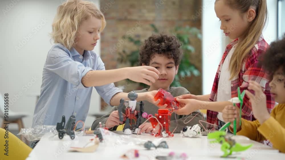 Enthusiastic kids assembling and programming robots during STEM class together with young female teacher Enthusiastic kids assembling and programming robots during STEM class together with young female teacher