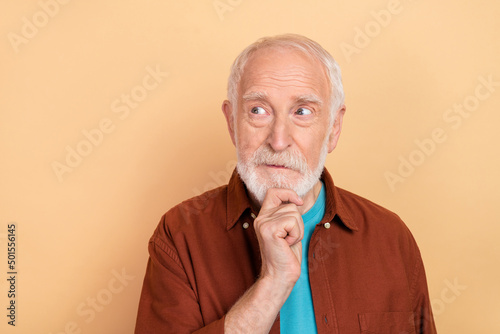 Photo of thinking old grey hairdo man look empty space wear brown shirt isolated on beige color background