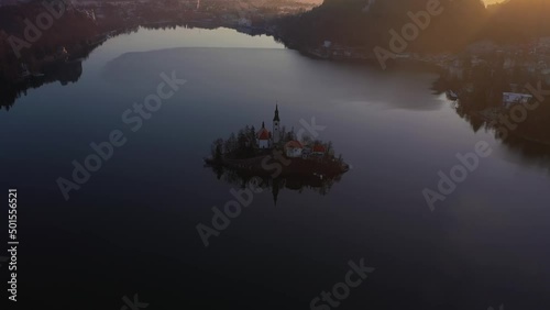 Bled Lake and Marijinega Vnebovzetja Church at Sunrise. Golden Hour. Hills and Forest. Slovenia, Europe. Reflection in Lake. Aerial View. Drone Flies Forward, Tilt Down photo