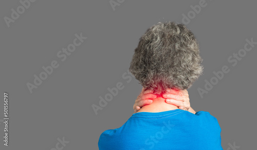 Back view of a senior woman suffering neck pain and neck tilt while standing against a gray background photo