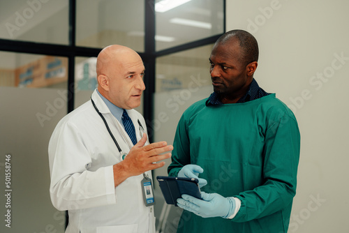 Male Surgeon and Doctor talking in hospital, They Consult Digital Tablet Computer while Talking about Patient's Health.