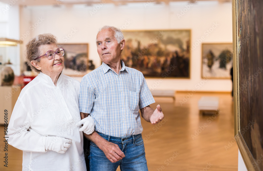 mature European couple examines paintings in an exhibition in hall of art museum mature European couple examines paintings in an exhibition in hall of art museum