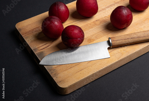 Red plums on bread board with knife and black background