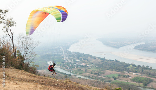 Paragliding in the sky. Paraglider flying over Landscape from Beautiful View Mekong River at Wat Pha Tak Suea in Nongkhai, Thailand.Aerial view. Concept of extreme sport, taking adventure/ challenge.