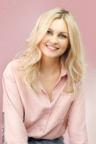 Blond woman in casual style. Girl in a shirt and with tousled hair. Blond woman in pink colors. Pastel colors and a girl. Girl smiles widely. Beautiful blonde and pink.