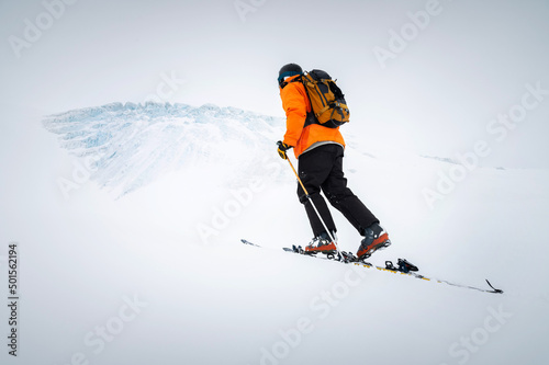 Winter skitour freeride in cloudy weather, snow-capped mountains against the backdrop of a glacier. Skier man in full gear climbs uphill in a skitour photo