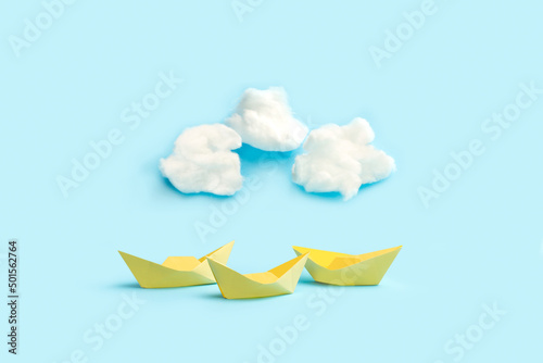 Barcos de papel amarillos junto a unas nubes esponjosas de algodón sobre un fondo celeste pastel liso y aislado. Vista de frente y de cerca. Copyspace photo