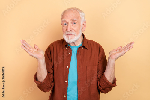 Photo of unsure old white hairdo man shrug shoulders wear brown shirt isolated on beige color background photo