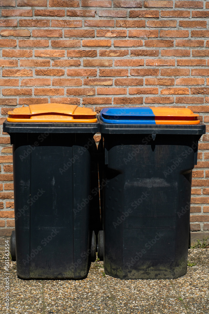 Rubbish bins for segregation plastic and paper to further recycle. Black trash cans for one household on brick wall background.
