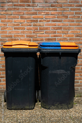 Obraz na płótnie Rubbish bins for segregation plastic and paper to further recycle. Black trash cans for one household on brick wall background. w salonie