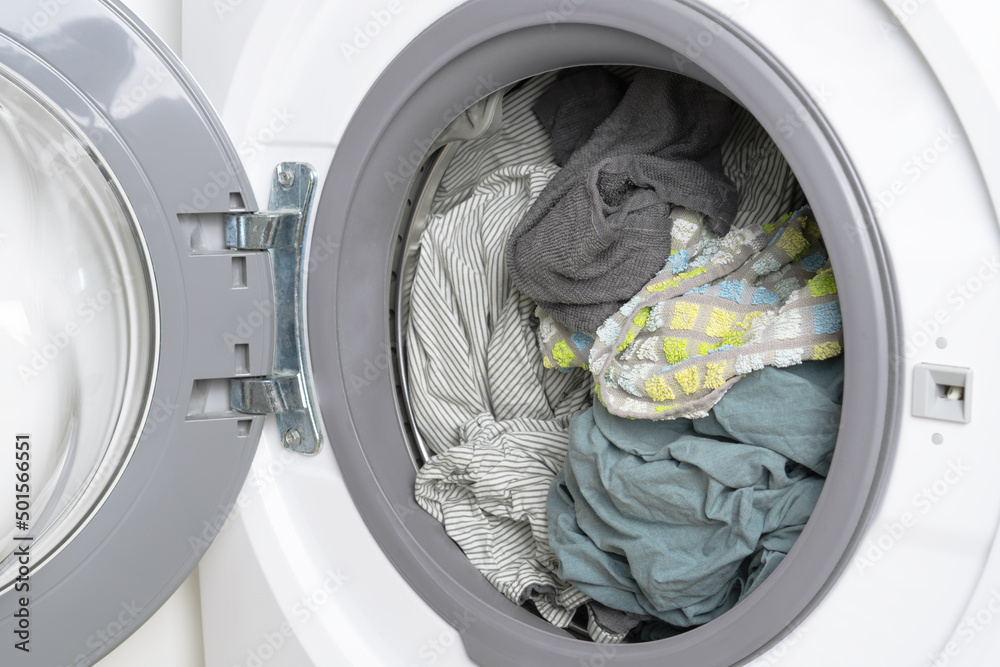 Washed cotton bed linen and towels in washing machine drum, close up. Washed cotton bed linen and towels in washing machine drum, close up.