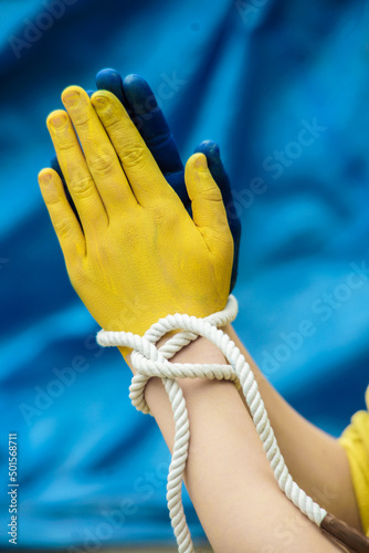 Children against war. Russia's invasion of Ukraine, a request for help from the world community. The child's hands are painted in yellow and blue, a gesture of faith and hope - praying on a blue backg
