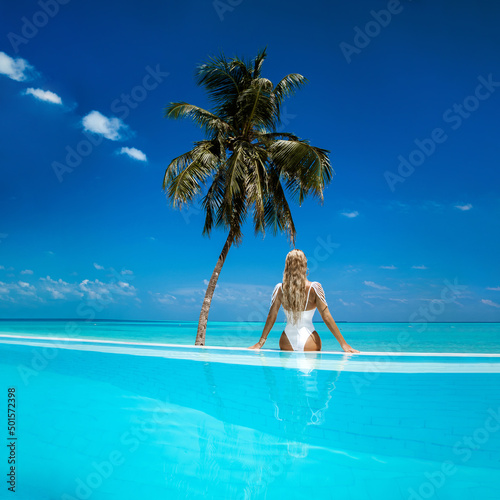 Elegant tanned woman in white swimsuit in pool on tropical Maldives island. Beautiful bikini body girl in pool with view on horizon. Sexy model near the pool on beautiful Indian ocean landscape.Travel
