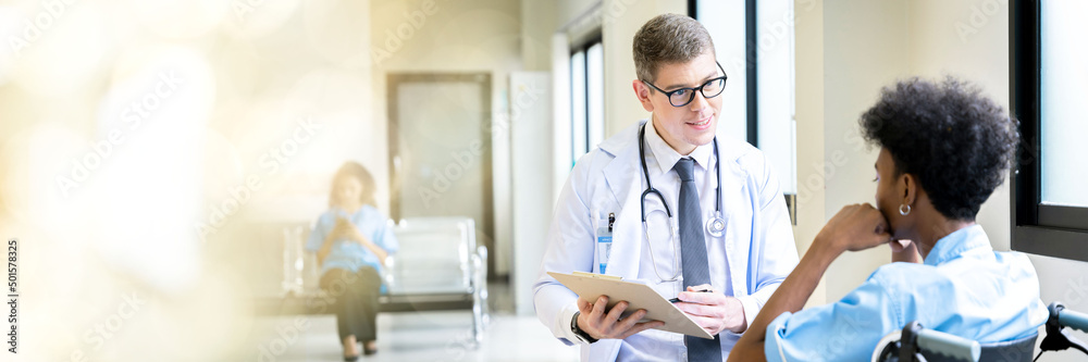 Obraz premium Web banner A male doctor takes a male patient who is admitted at the hospital for a walk through the window corridors of the hospital for psychotherapy. by having the patient sit in a wheelchair